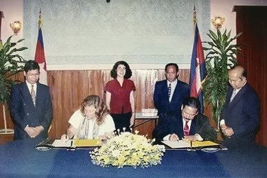 Registering the University of the Nations Cambodia as an NGO in 2002 — two people signing documents at a table under Cambodian flags
