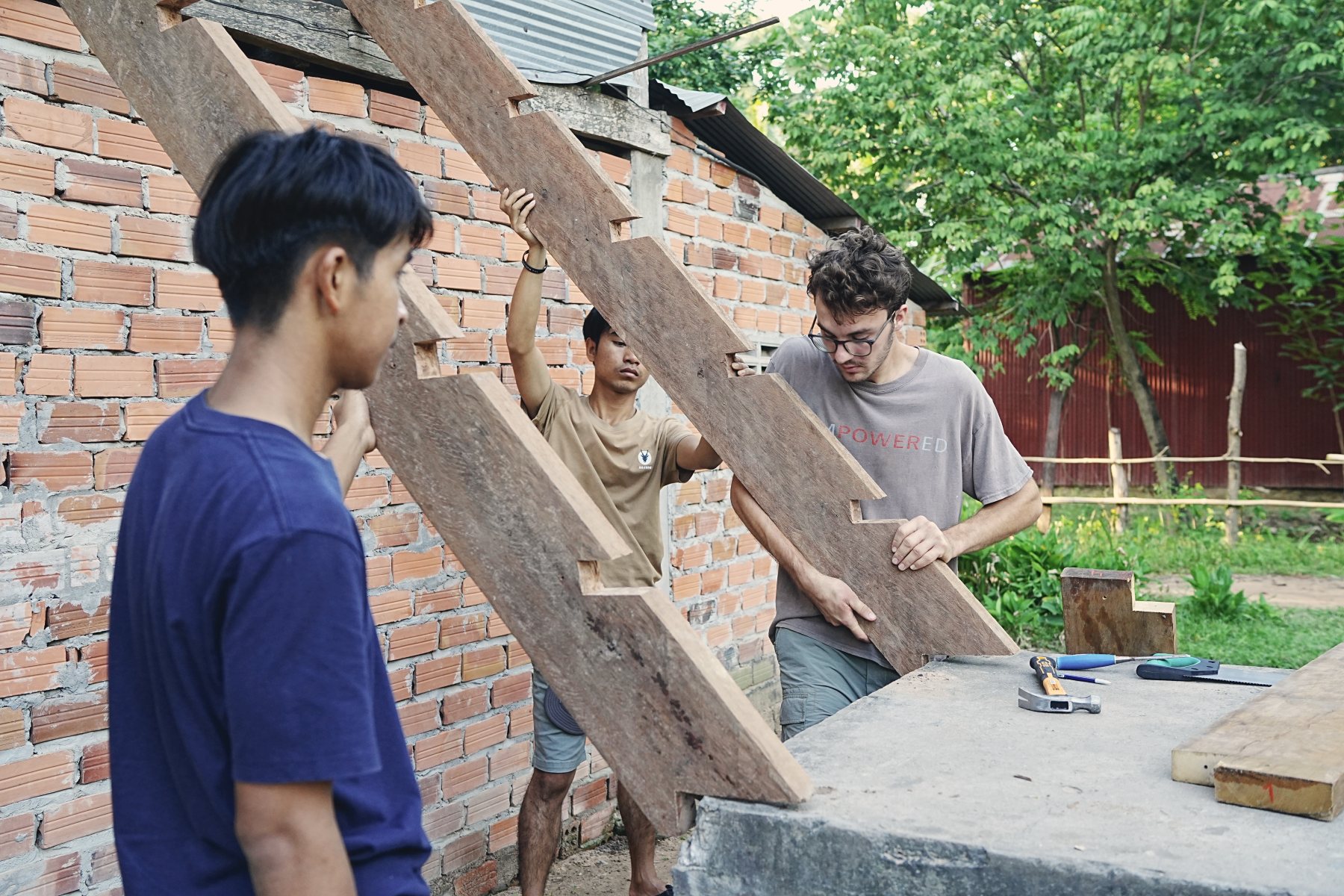 Three young men fitting a wooden staircase against a brick wall