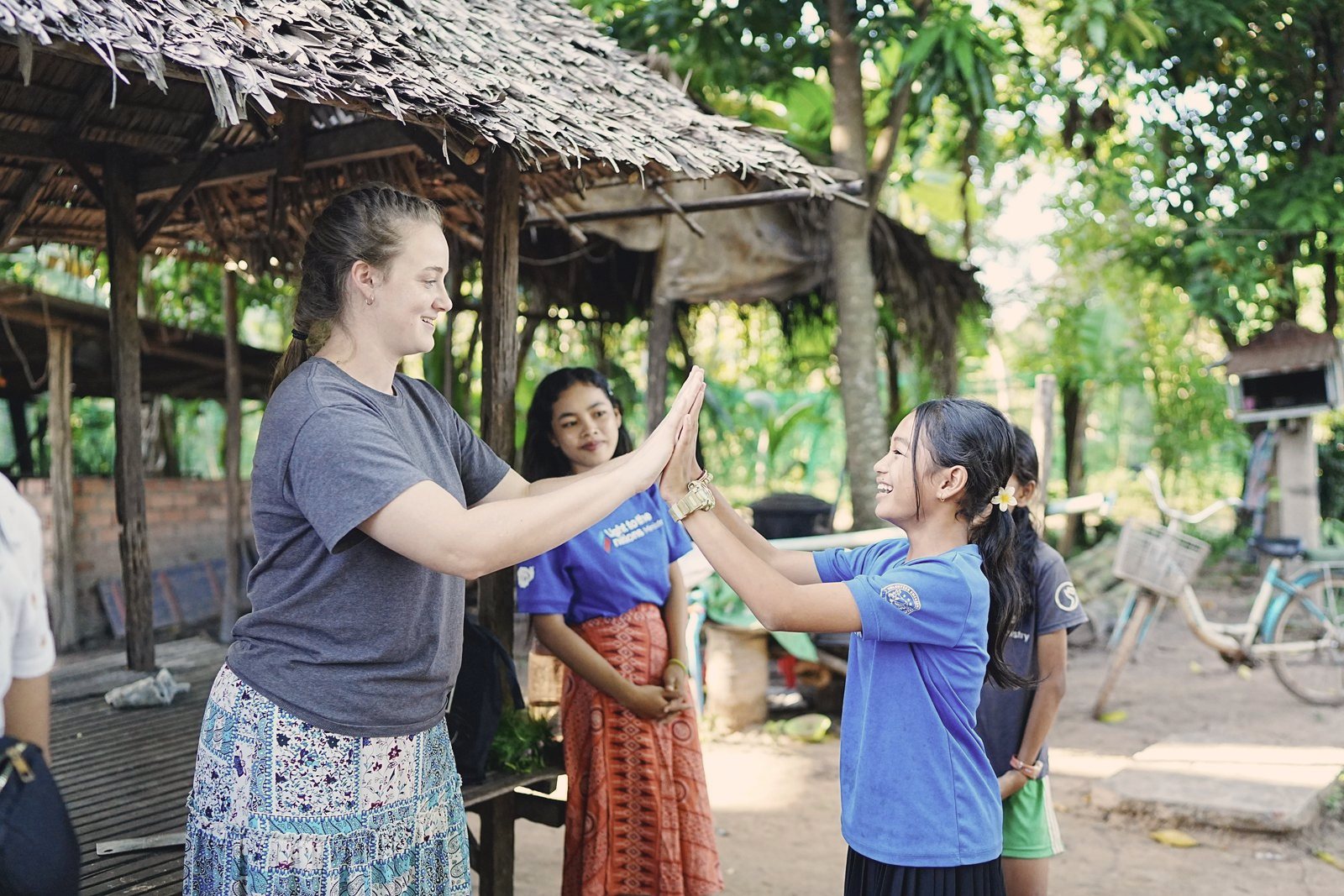 A visiting student high-fiving a laughing girl in a village