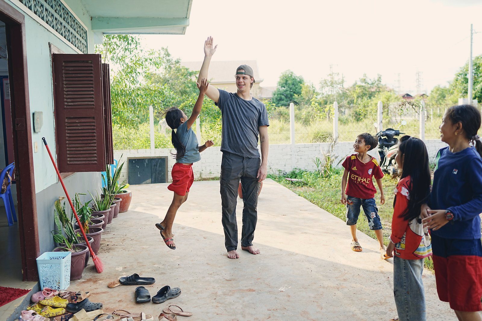 A visiting team member high-fiving a leaping boy outside a village house