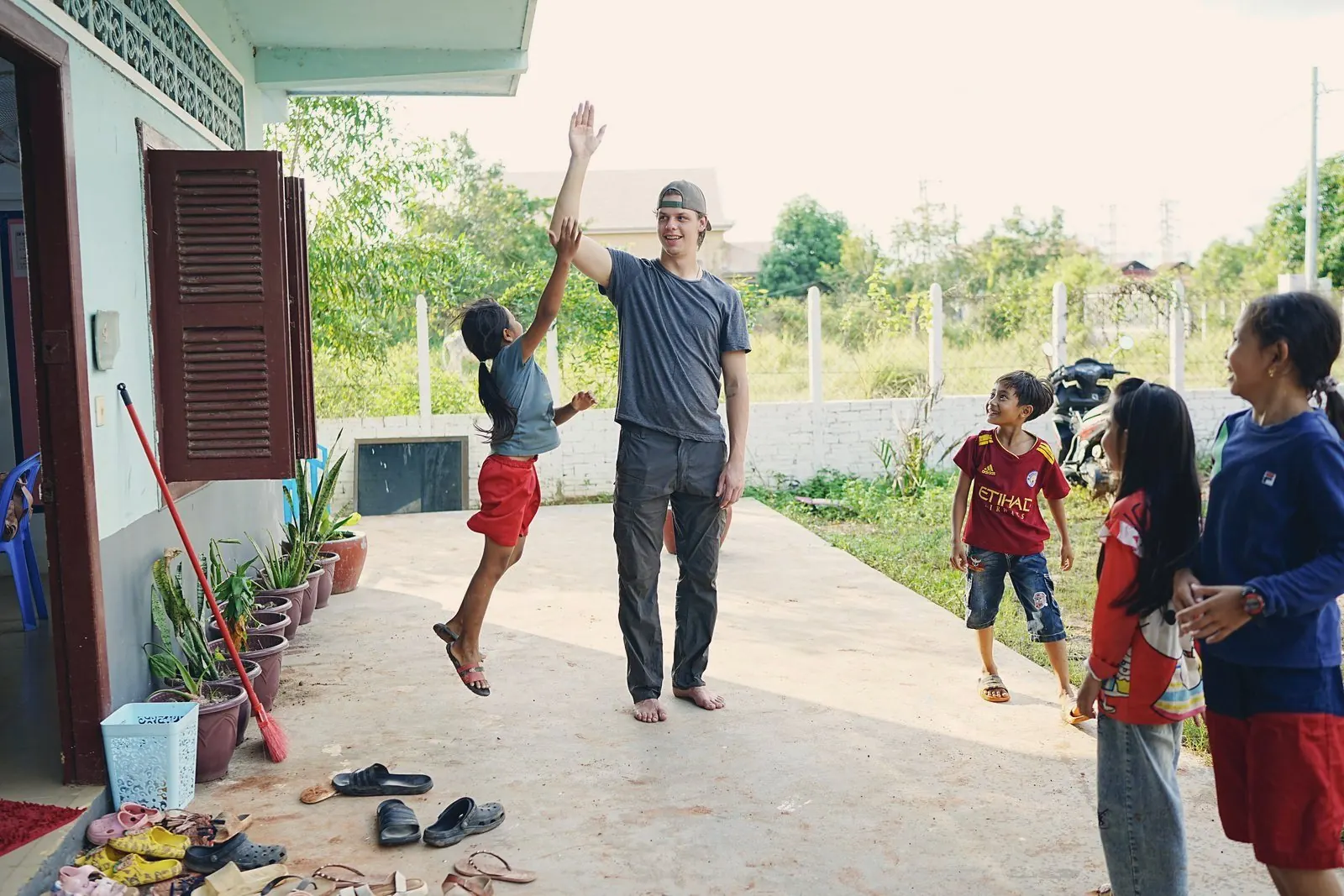 A visiting team member high-fiving a leaping boy outside a village house