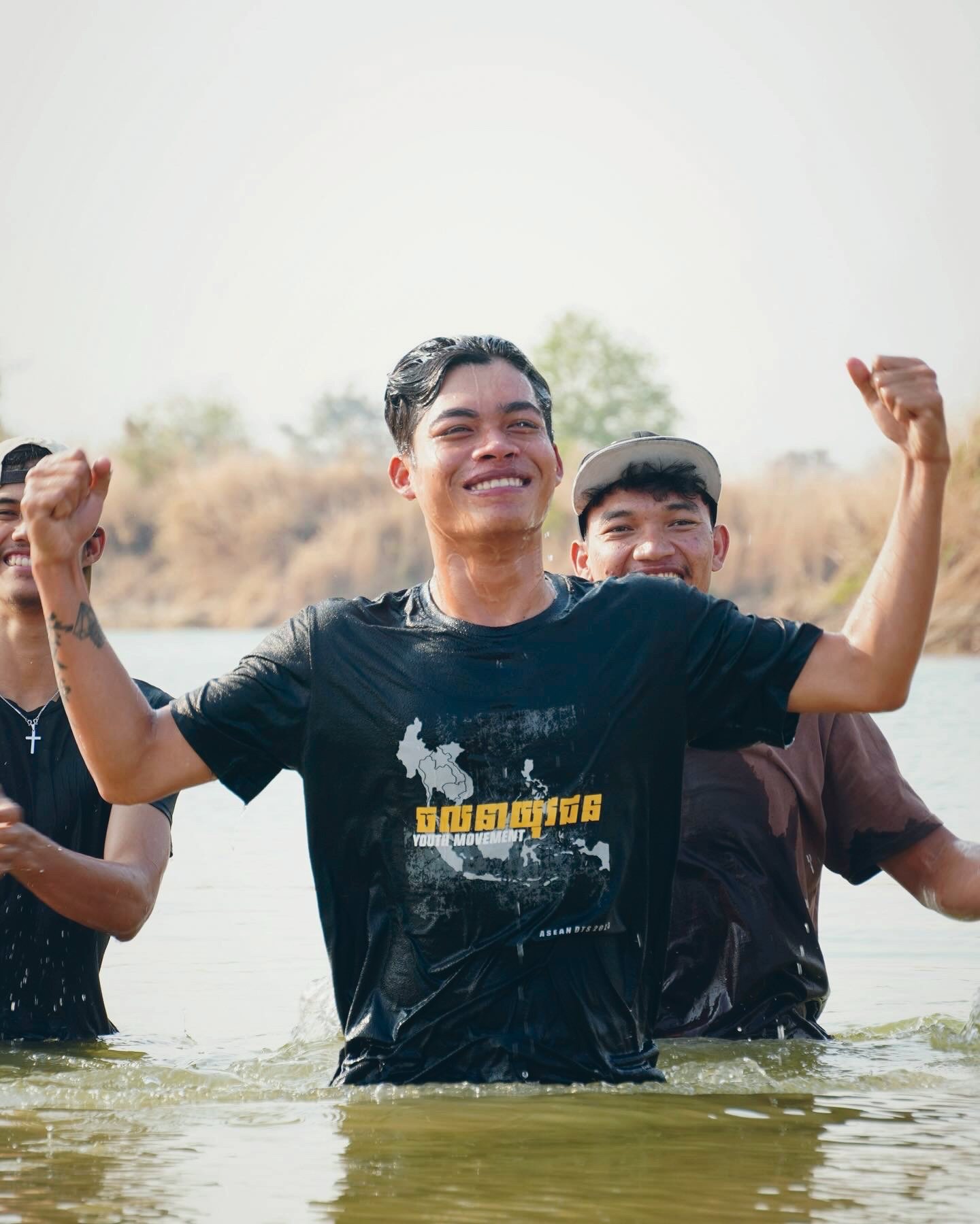 A young man celebrating in the river just after his baptism, friends beside him
