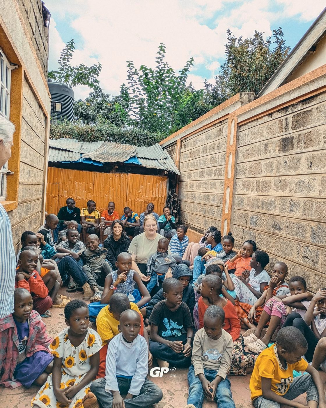 DTS students sitting among dozens of children in a school courtyard on outreach