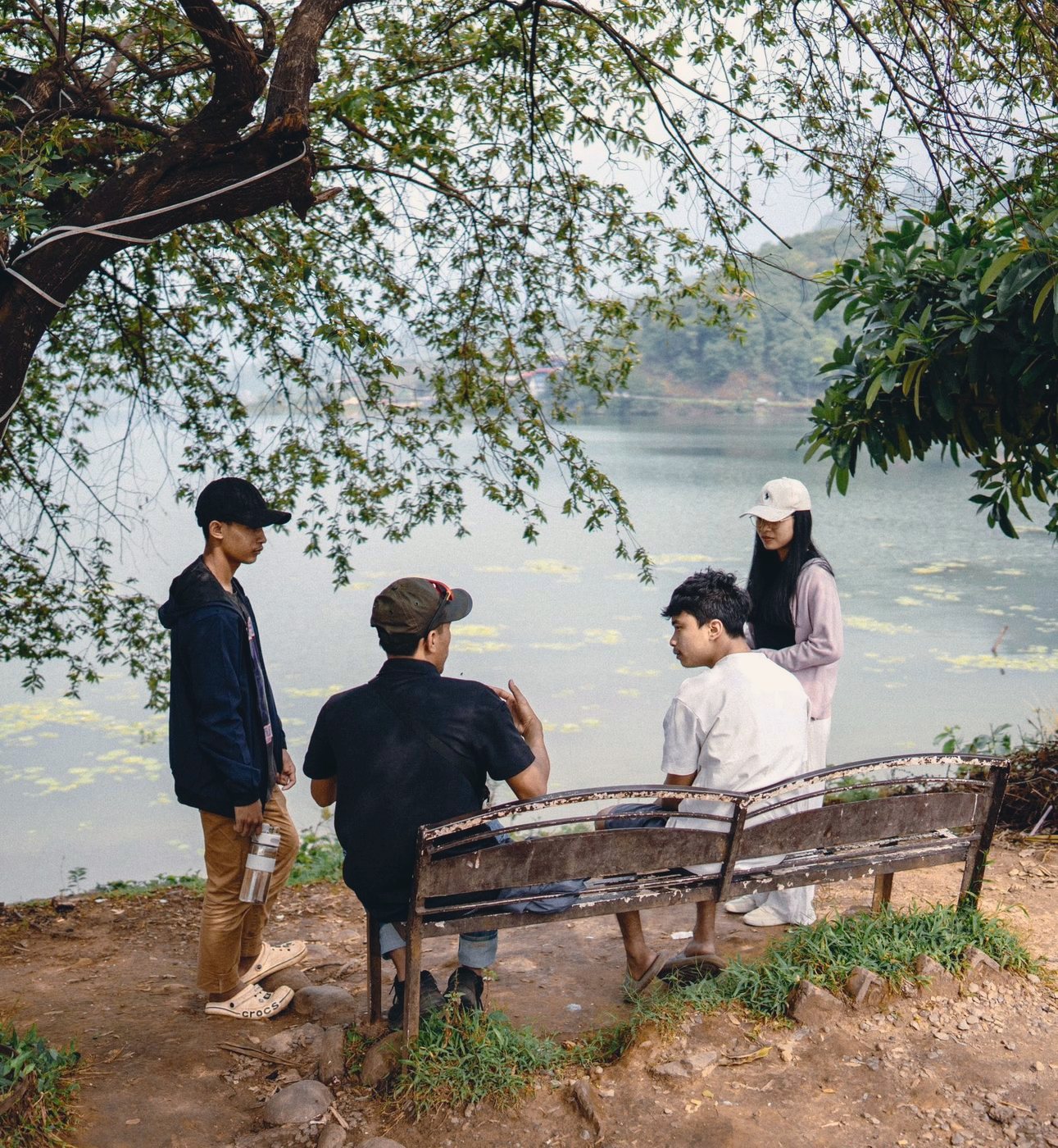 Four DTS students talking on a bench beside a lake on outreach