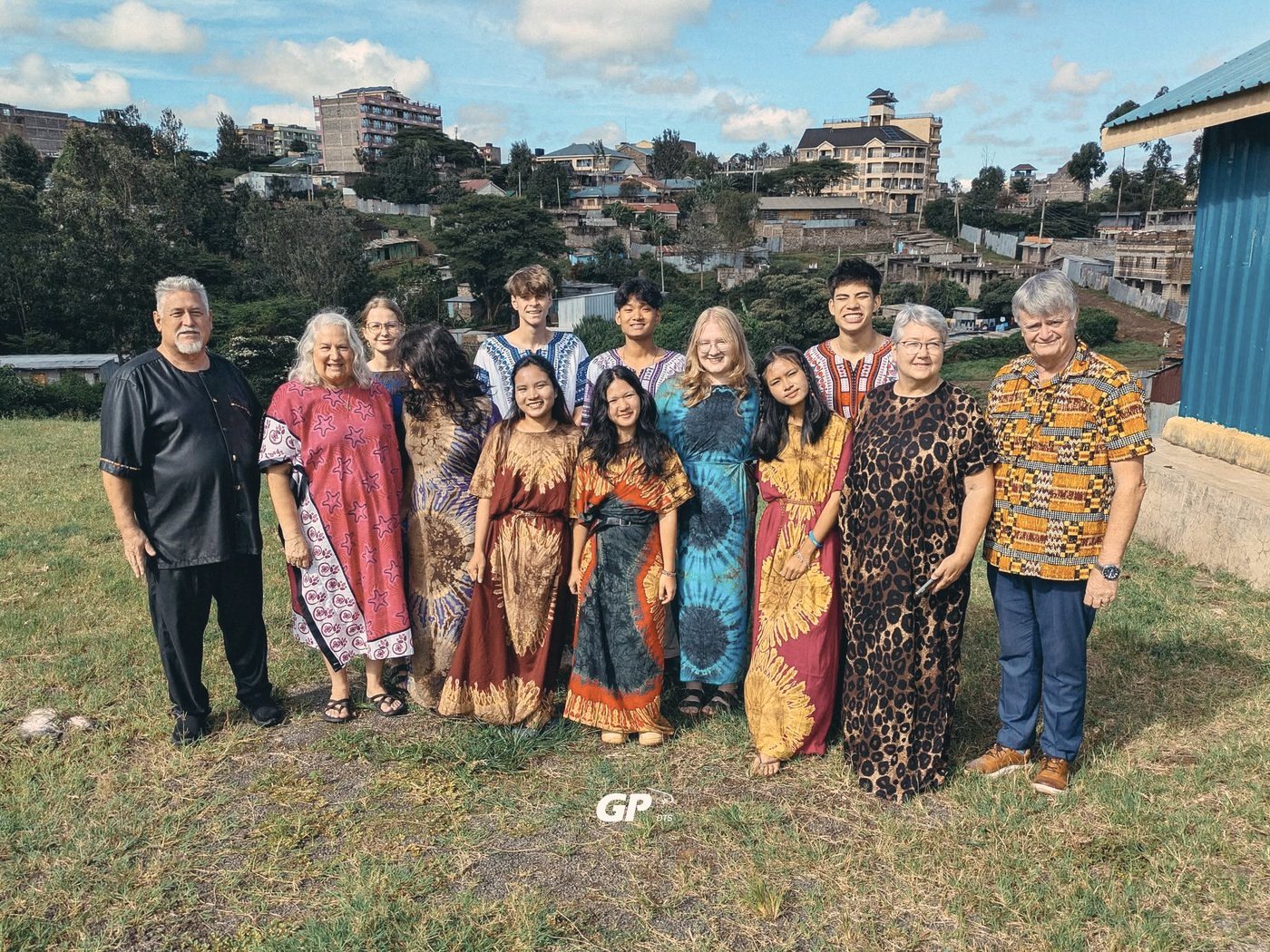 A DTS outreach team in bright traditional dresses and shirts, standing on a hillside above a town