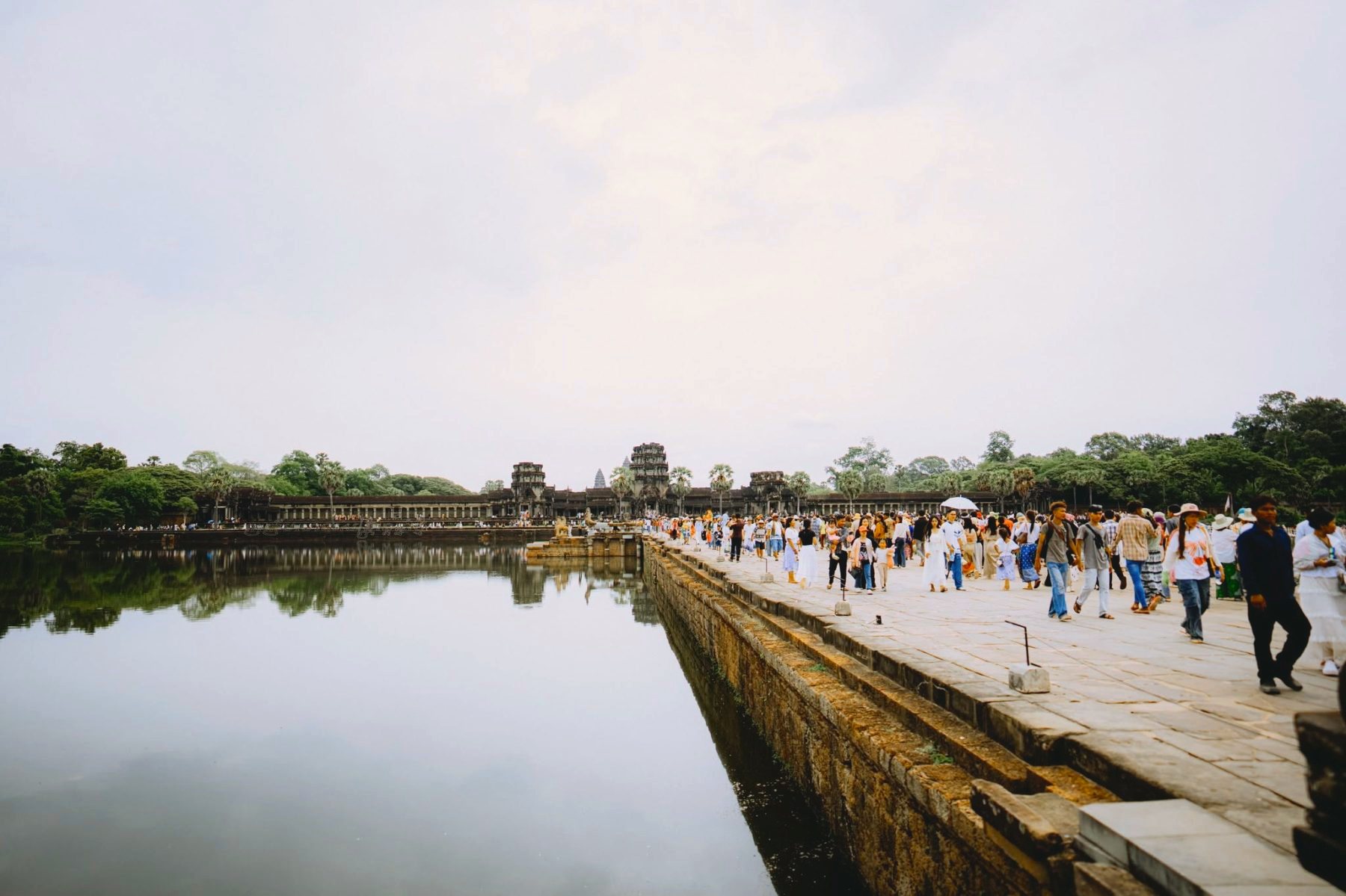 Visitors walking the long stone causeway across the moat toward Angkor Wat